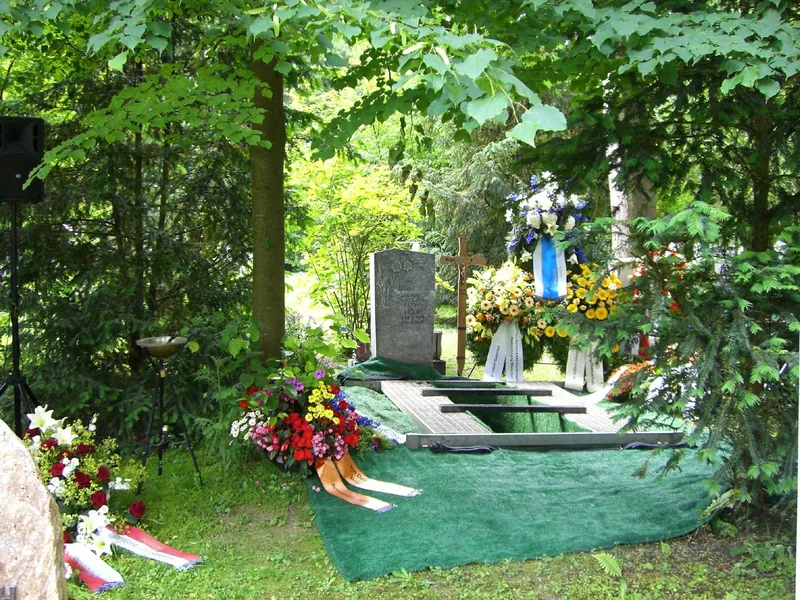 Erdbestattung – Grab mit Kränzen und Blumenschmuck im Wald