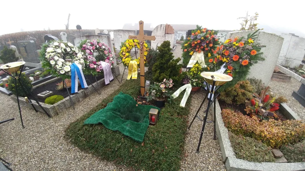 Feuerbestattung – Urnengrab mit Kränzen und Holzkreuz auf dem Friedhof